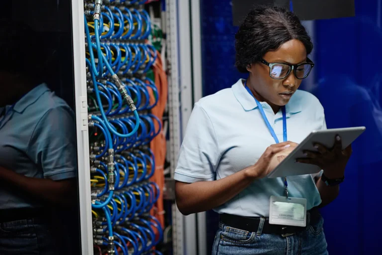 Technician with a tablet working at an open server rack with blue patch cabling