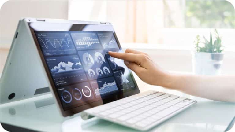 Hand using a touchscreen laptop displaying a data dashboard on a desk