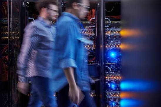 Two professionals walking past illuminated server racks in a data center