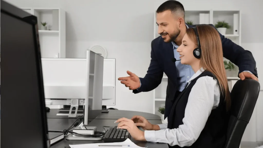 IT specialist helping an employee at a desktop workstation in a financial office