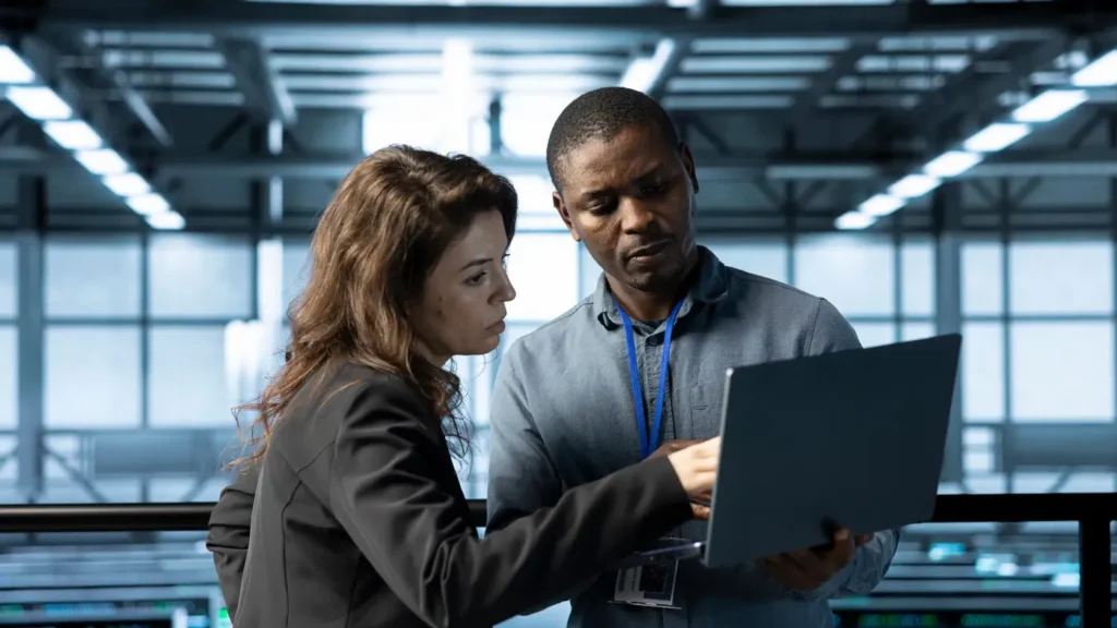 Two colleagues in a server room planning industry-specific IT services on a laptop