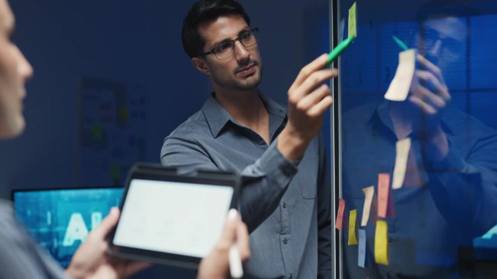 Consultant at an engineering or architecture firm reviewing project notes on a glass wall while a colleague holds a tablet