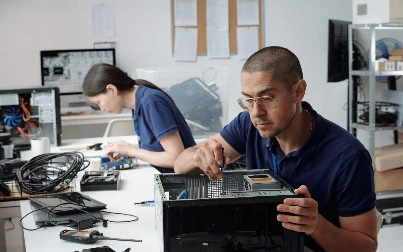 Two technicians at a workbench disassembling small electronic devices
