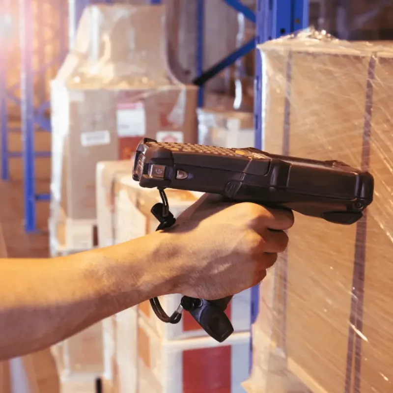 Handheld barcode scanner reading a shipping label on wrapped pallets in a warehouse